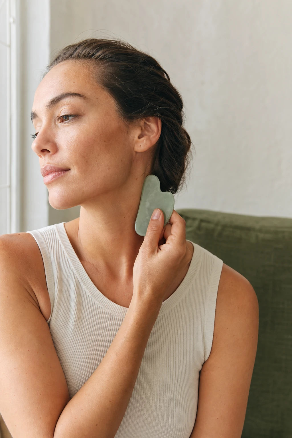 Woman gently using a jade gua sha tool along her neck